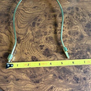 May include: A gold-colored lamp harp with a measurement of approximately 7 inches. The harp is curved and has a connector at each end. The background is a brown, wood-grain surface.