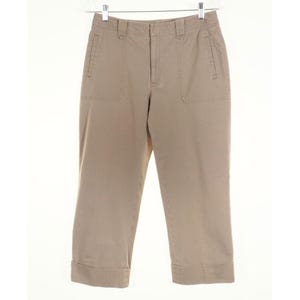 May include: Tan-colored cropped pants with a classic design. The pants feature two front pockets, belt loops, and a button and zipper closure. The cuffs are folded up. The pants are hanging on a clear hanger.