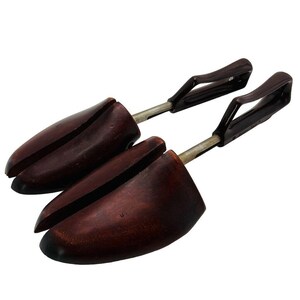 May include: Two dark brown wooden shoe trees with metal rods and dark brown handles. The shoe trees are designed to maintain the shape of shoes and absorb moisture.