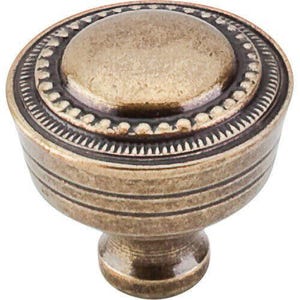 May include: A bronze-toned cabinet knob with a detailed design. The knob features a rounded top with concentric circles and a decorative edge. The base has a cylindrical shape with horizontal grooves, and a short, rounded stem.