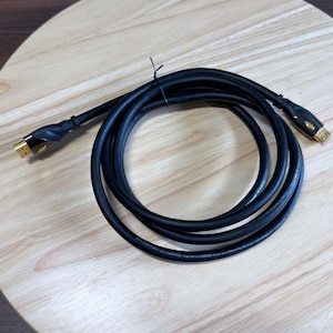 May include: A black Monster Ultimate High Speed HDMI cable with Ethernet featuring gold-plated connectors on both ends. The cable is coiled in a circular shape and includes black plastic housing around the connector heads with branding text.
