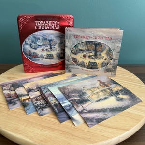 Puede incluir: Una colección con temática navideña que presenta una lata roja y una funda de CD, ambas con la etiqueta "Treasury of Christmas". La lata y la funda de CD muestran una escena de un pueblo invernal. También se incluyen varias impresiones artísticas con escenas de paisajes invernales.