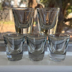 Può includere: Set di sei bicchieri da shot in vetro trasparente con bordo bianco. I bicchieri sono impilati uno sopra l'altro.