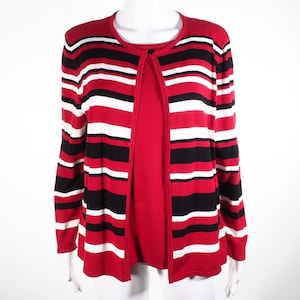 Könnte beinhalten: Eine langärmelige Strickjacke mit horizontalem Streifenmuster in Rot, Schwarz und Weiß, getragen über einem einfarbigen roten Oberteil. Die Strickjacke hat einen Rundhalsausschnitt und einen einzelnen Knopfverschluss oben mit durchgehendem Muster.