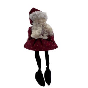 May include: A decorative Santa Claus doll with a burgundy dress and hat, adorned with gold stars. The doll has a white beard and hair, and black legs with black shoes. A festive Christmas decoration.