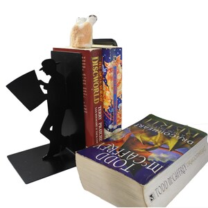 May include: Black metal bookends shaped like a person reading a newspaper. The bookends are holding up two books, one with the title "The Science of Discworld" and the other with the title "Dragonflight".