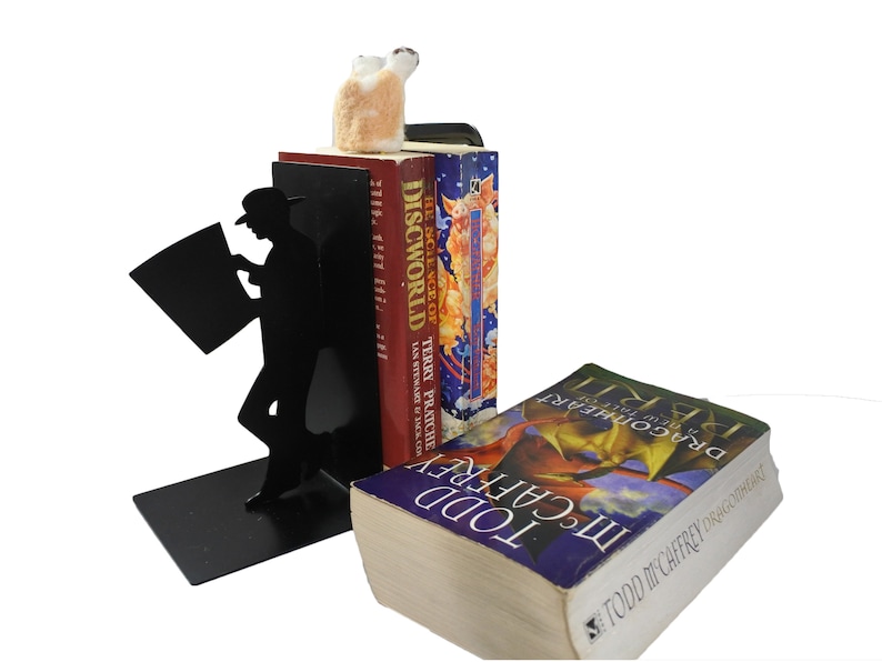 May include: Black metal bookends shaped like a person reading a newspaper. The bookends are holding up two books, one with the title "The Science of Discworld" and the other with the title "Dragonflight".