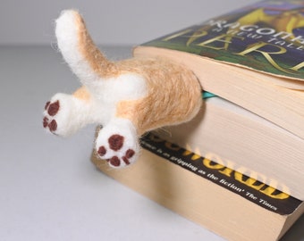 May include: A felt bookmark shaped like a dog's rear end with brown paw prints. The bookmark is sticking out of a stack of books. The top book has the title "Dragonheart: A New Tale of  " on the cover.