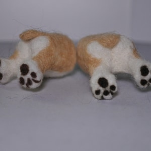 May include: Two small, felted, cream-coloured dogs with black paw prints, lying on their backs with their legs in the air.