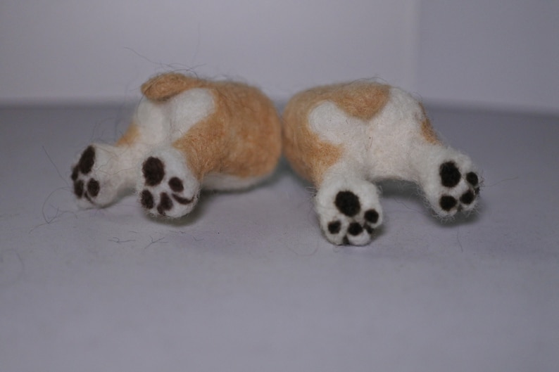 May include: Two small, felted, cream-coloured dogs with black paw prints, lying on their backs with their legs in the air.