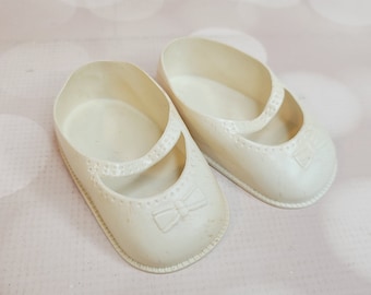 May include: A pair of white plastic baby shoes with a bow detail on the front.