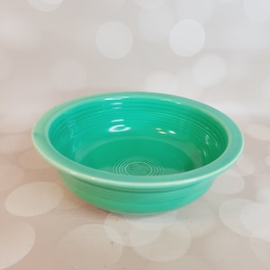 May include: A turquoise ceramic bowl with a rounded rim and a smooth, glossy finish. The bowl has a series of concentric circles on the inside.
