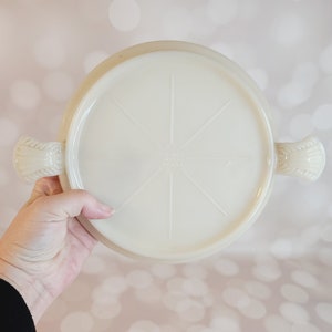 Puede incluir: Plato para pastel de vidrio blanco con un borde elevado y dos asas. El plato tiene un diseño de estrella en la parte inferior.