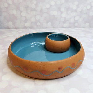 May include: A terracotta ceramic serving dish with a blue glazed interior and a smaller matching bowl. The dish has a wavy rim with pink accents.