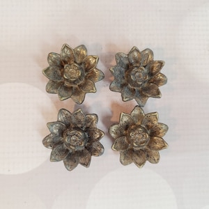 Puede incluir: Cuatro candelabros de metal de color dorado en forma de flor. Cada candelabro tiene un diseño en relieve en el centro.