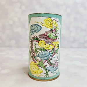 Peut inclure: Un récipient cylindrique peint à la main avec un bord et une base turquoise. Le récipient présente un motif de dragon coloré avec des accents jaunes, roses, verts et bleus. Le dragon est placé sur un fond blanc avec des nuages stylisés.