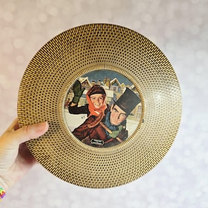 May include: Vintage round picture frame with a woven, textured border. The frame holds a winter scene illustration of a couple in winter attire. The illustration features a man in a top hat and a woman with a red scarf.