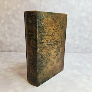 May include: A rectangular, vintage-style book with a map design. The cover features a detailed, aged map in shades of brown and gold, with a compass rose at the center. The book's edges show wear, enhancing its antique appearance.