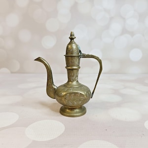 May include: A small, ornate brass teapot with a lid and a handle. The teapot is decorated with intricate floral patterns.