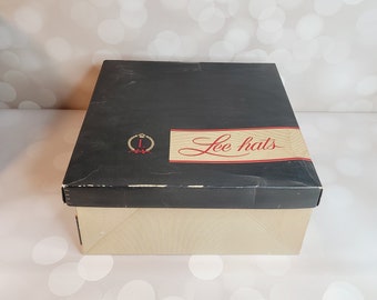 May include: A black box with a cream-colored bottom. The box has a gold crown and the text "Lee Hats" in red lettering.
