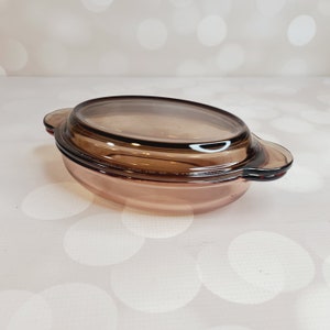 May include: A brown glass baking dish with a lid. The dish has a rounded shape and two handles on the sides.