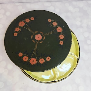 Puede incluir: Un juego de fuentes vintage con una tapa verde oscuro con un diseño floral en coral y dorado. El juego incluye un recipiente redondo y cuatro fuentes de color verde amarillento. La tapa está ligeramente entreabierta, revelando las fuentes.