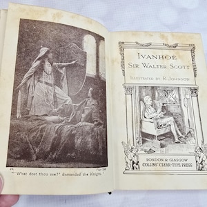 May include: An open book with illustrations from "Ivanhoe" by Sir Walter Scott. The left page features a sepia-toned illustration of a woman in a long dress, while the right page displays the title and author, with a drawing of a man at a desk.