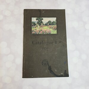 May include: A vintage catalog with a dark brown cover. The cover features a landscape painting of a garden with pink flowers and trees. The text "Catalogue I 1926" is printed on the cover.