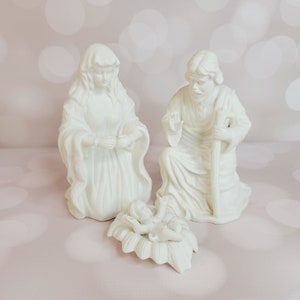 Puede incluir: Escena de la natividad de porcelana blanca con María, José y el niño Jesús. Las figuras están arrodilladas y el bebé está acostado en un pesebre.