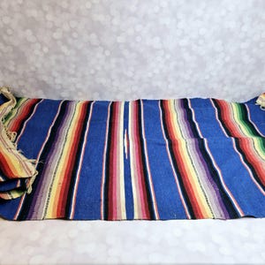 May include: A colorful striped woven blanket with a blue background. The blanket has stripes of red, yellow, orange, pink, purple, and green.
