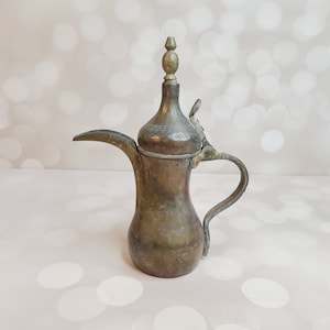 Könnte beinhalten: Eine antike arabische Kaffeekanne aus Messing mit einem Scharnierdeckel und einem dekorativen Knauf. Die Kanne hat eine abgenutzte, gealterte Patina und ein traditionelles Design.