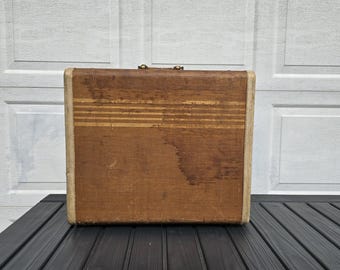 May include: A vintage brown suitcase with a white trim and a striped pattern. The suitcase has a worn look and is made of a fabric material.