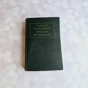 Könnte beinhalten: Ein grünes Hardcover-Buch mit dem Titel "TABER'S CYCLOPEDIC MEDICAL DICTIONARY" in goldenen Lettern.