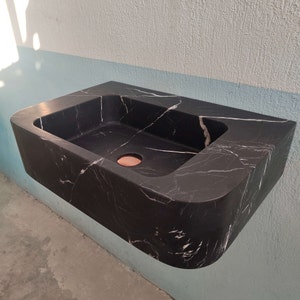 May include: A black marble bathroom sink with a white veined pattern. The sink is wall-mounted and has a round drain.