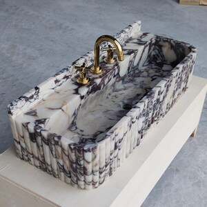 Custom Calacatta Viola marble sink with no faucet holes, designed for seamless integration with wall-mounted fixtures.