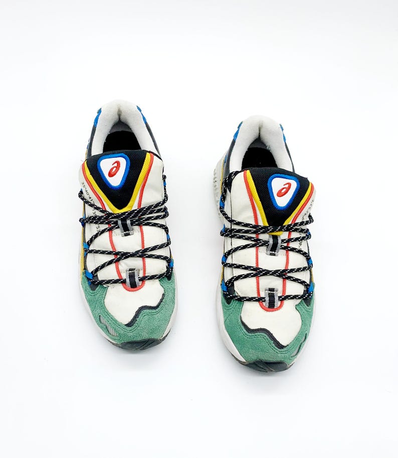 May include: A pair of white sneakers with green, blue, yellow, and black accents. The sneakers have a lace-up closure and a chunky sole.