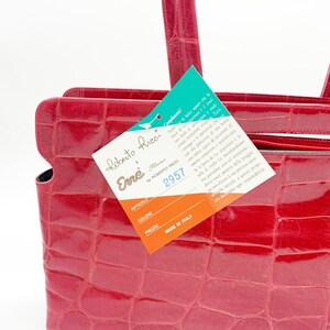May include: A red crocodile embossed leather handbag with a top handle and a tag that reads "Roberto Ricci Enne Florence by Roberto Ricci 2957 Made in Italy".