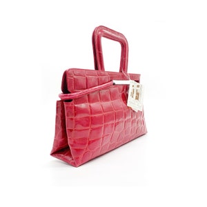 May include: A red crocodile embossed leather handbag with a top handle and a silver metal accent. The bag has a small tag attached to it.