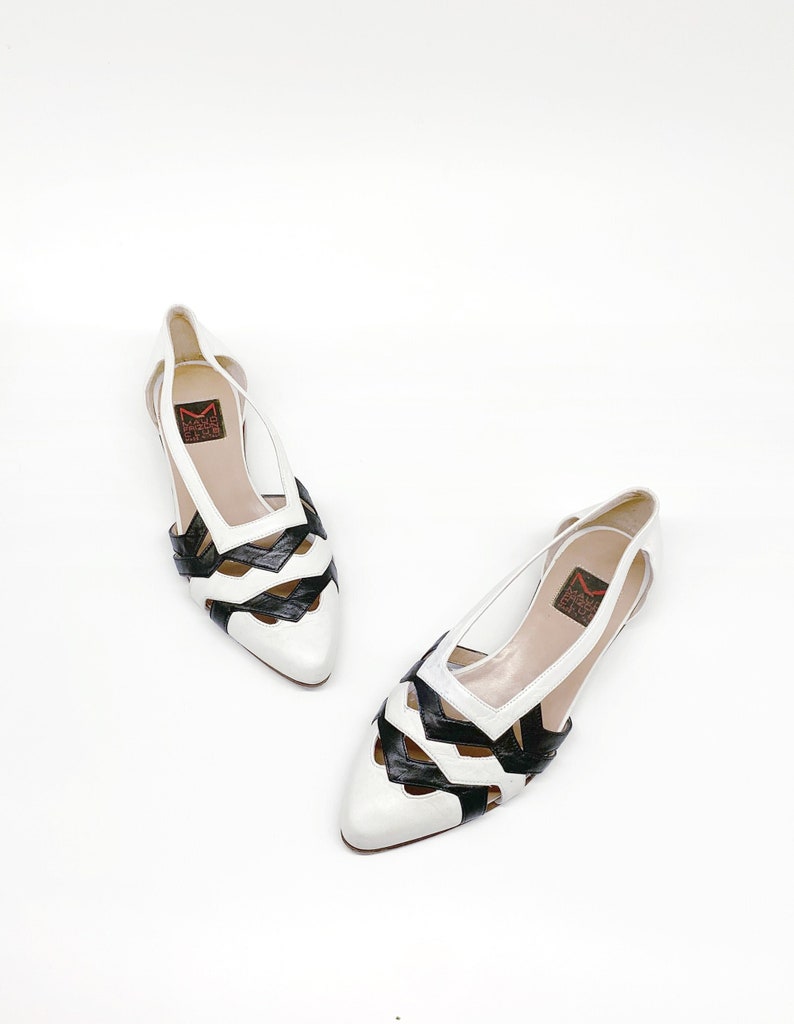 May include: A pair of white and black leather shoes with a cut-out design. The shoes have a pointed toe and a low heel. The brand name "Mario Valentino" is visible on the insole.