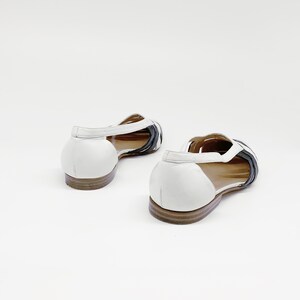 May include: A pair of white leather sandals with black leather straps. The sandals have a low heel and an open toe.