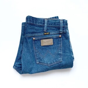 May include: A pair of blue denim jeans folded in half, showing the back pockets with a brown leather patch that reads "Wrangler".