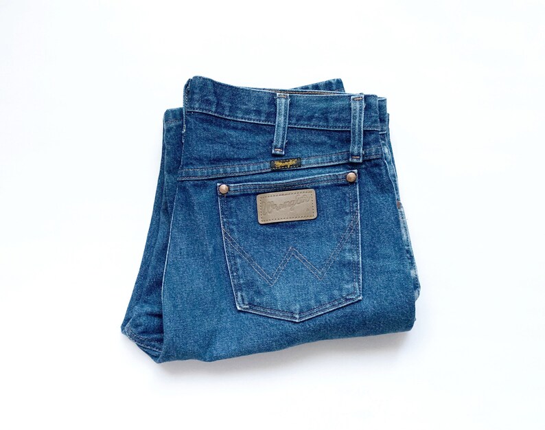 May include: A pair of blue denim jeans folded in half, showing the back pockets with a brown leather patch that reads "Wrangler".