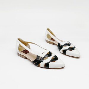 May include: A pair of white leather flats with black leather cutouts. The shoes have a pointed toe and a low heel.