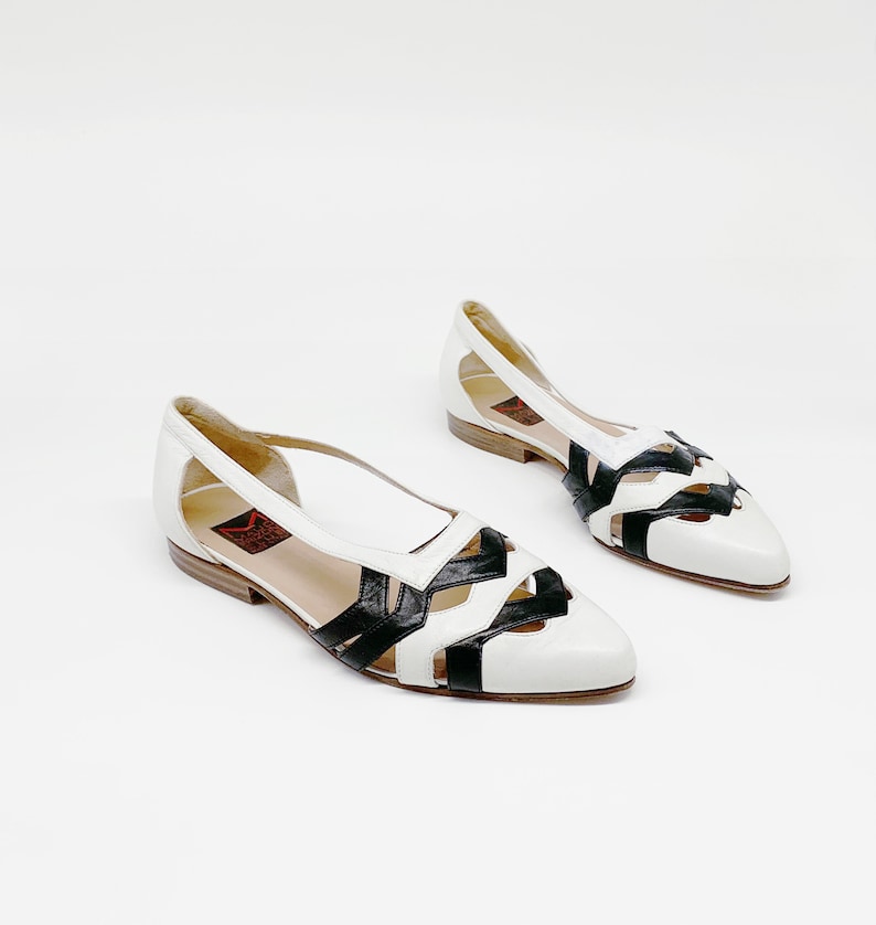 May include: A pair of white leather flats with black leather cutouts. The shoes have a pointed toe and a low heel.
