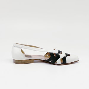 May include: White leather sandals with black leather straps and a cut-out design.