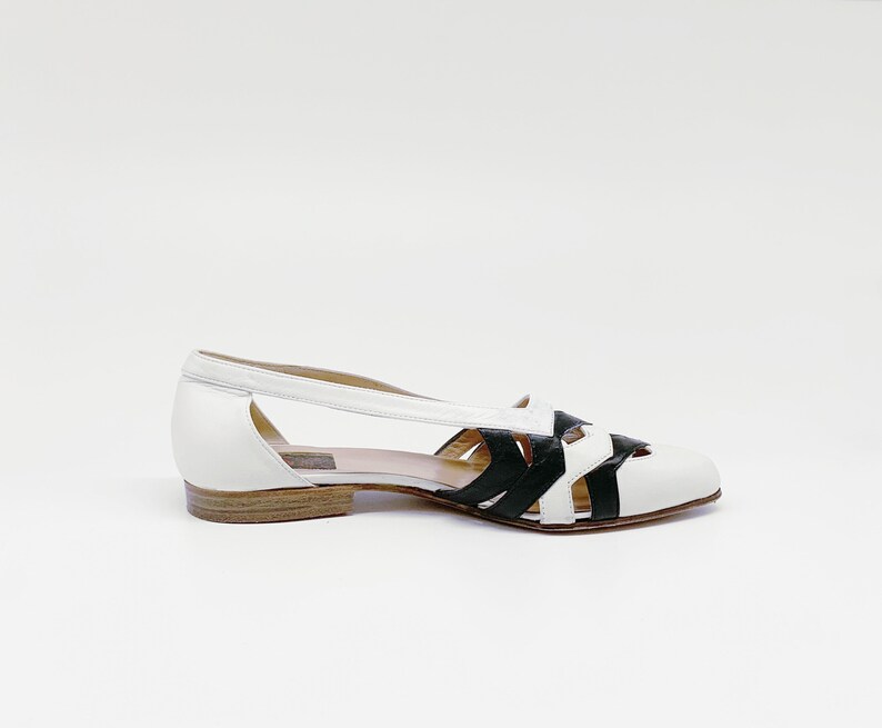 May include: White leather sandals with black leather straps and a cut-out design.