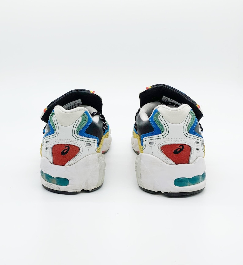May include: A pair of white, blue, black, and red sneakers with a velcro strap. The sneakers have a multi-colored design and a white sole.