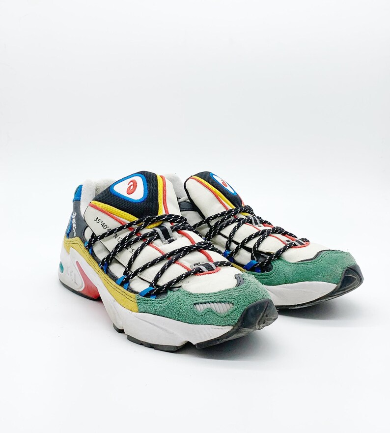 May include: A pair of white, green, yellow, blue, and black sneakers with black laces. The sneakers have a chunky sole and a logo on the side.