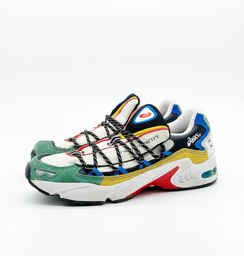 May include: White, green, yellow, blue, and red sneakers with black laces and a black and blue Asics logo on the side. The sneakers have a white sole with a red "GEL" logo.