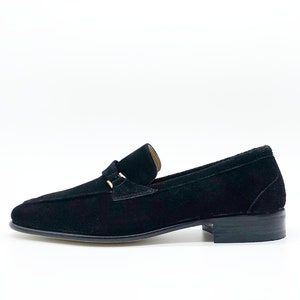 May include: Black suede loafers with a gold buckle detail. The loafers have a rounded toe and a low heel.